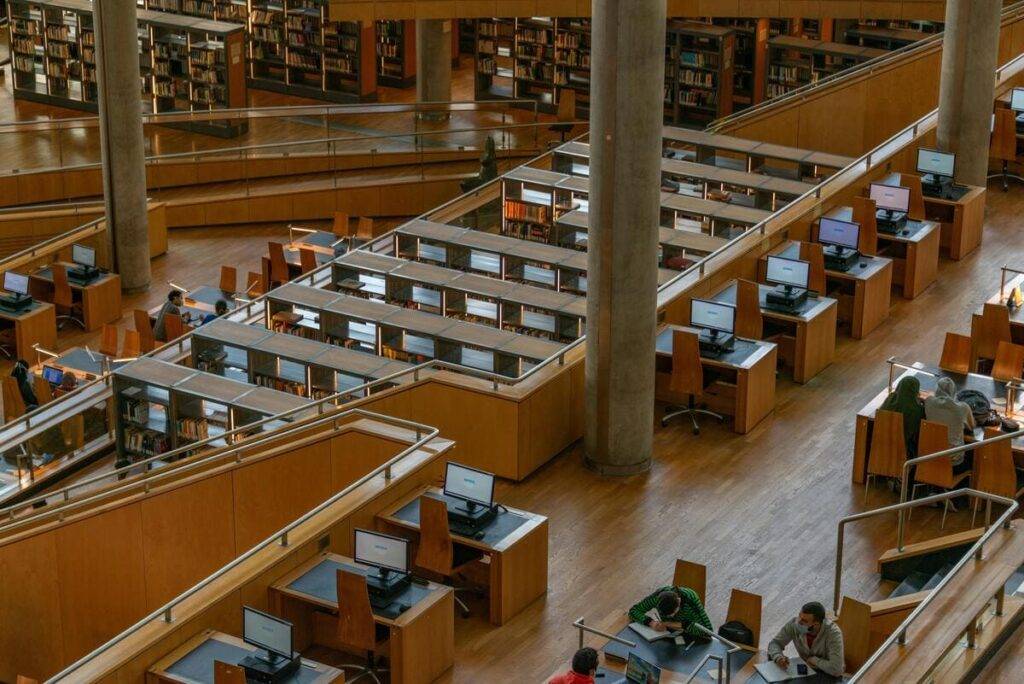 OpenSistemas - Consultora IT 71 Una biblioteca amplia y moderna, el espacio está organizado en varios niveles con estanterías llenas de libros y áreas de trabajo individuales equipadas con computadoras de escritorio.